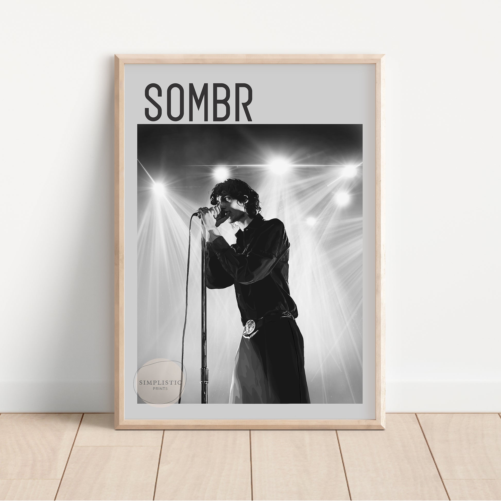 Framed poster of a person singing into a microphone with 'SOMBR' text above, on a light wooden floor.