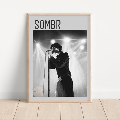 Framed poster of a person singing into a microphone with 'SOMBR' text above, on a light wooden floor.