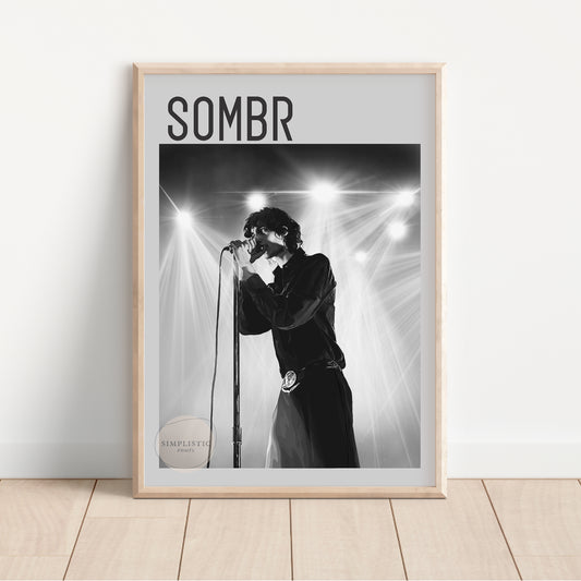 Framed poster of a person singing into a microphone with 'SOMBR' text above, on a light wooden floor.